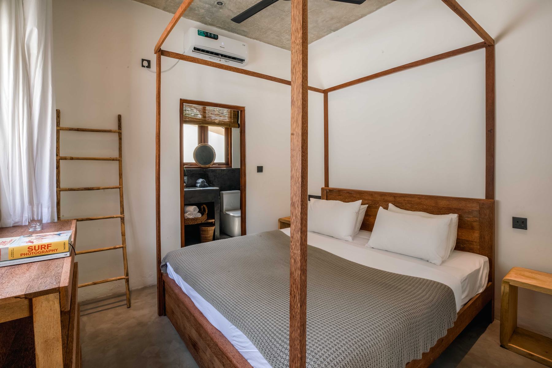 Second king bedroom with white walls, a four-poster teak bed, a bamboo towel ladder and the bathroom beyond