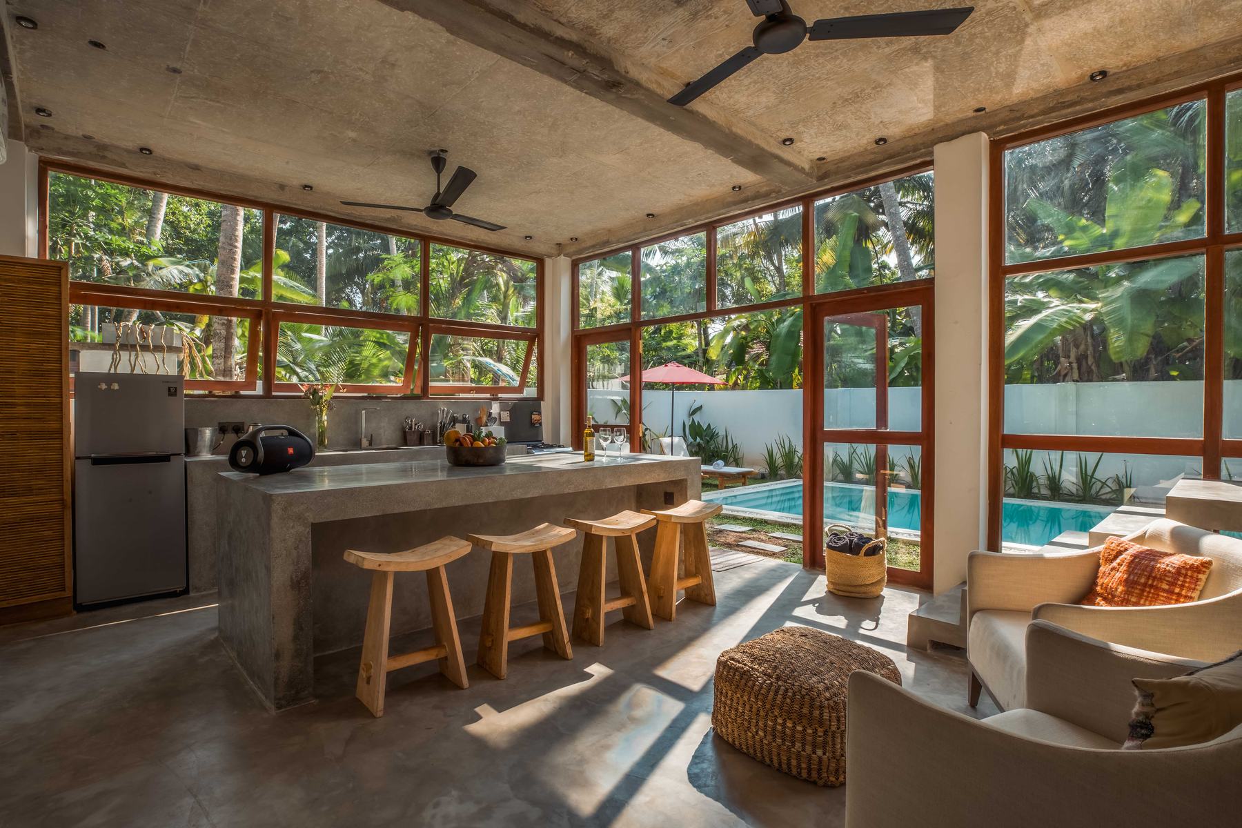 Open-plan kitchen and living room with bar stools, a sofa and floor-to-ceiling windows looking onto the pool