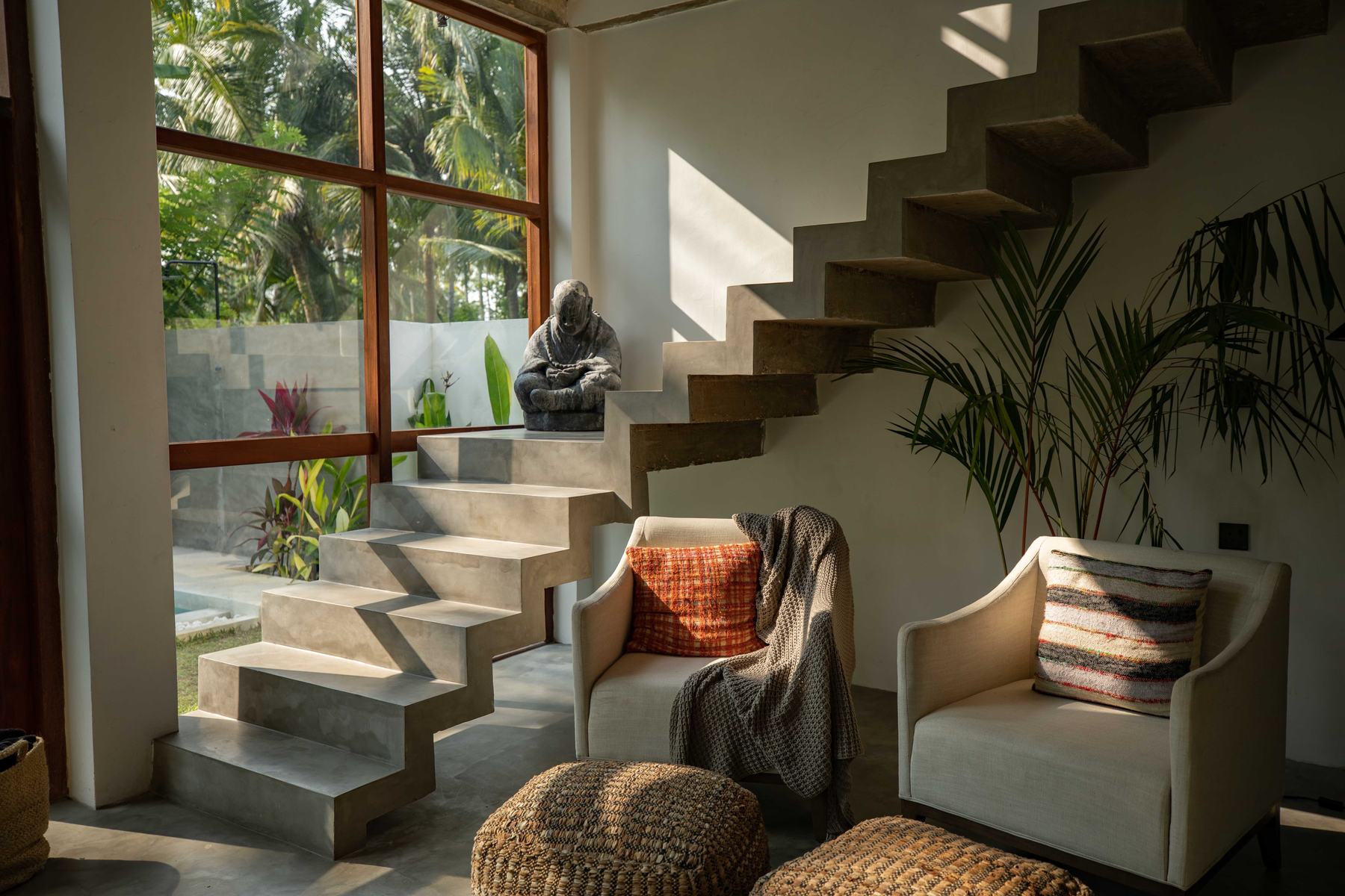 Floating concrete staircase beside two armchairs and a stone statue